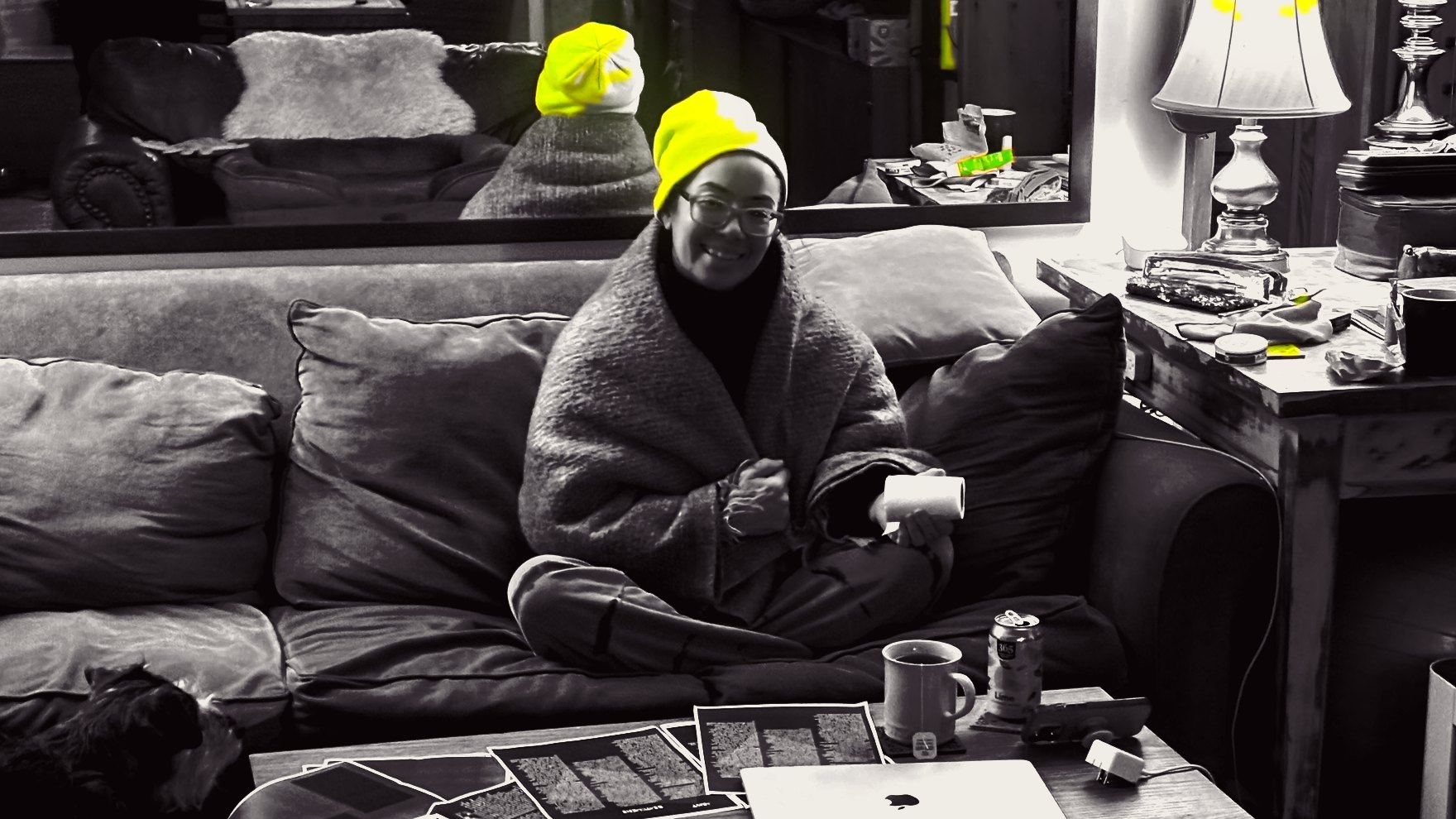 The same hero off duty: wrapped in a blanket on the couch in a glowing neon beanie, holding a roll of paper towels.